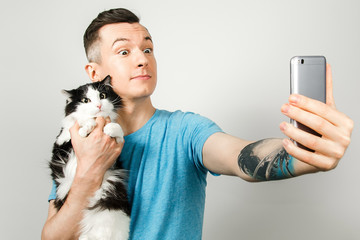 Young hipster does selfie with cat on light gray background.
