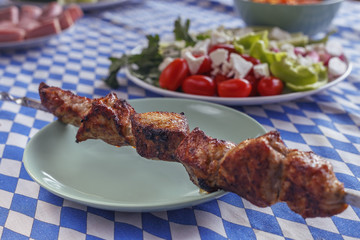 skewer with fried meat on a plate and of fresh salad close-up