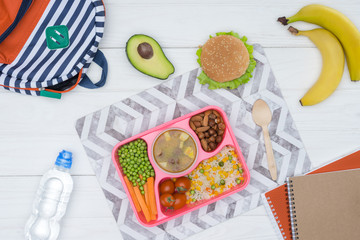 top view of tray with kids lunch for school and copybooks on wooden table