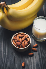 Almond milk in a glass with almond nuts and bananas on a wooden table. Healthy food and drink concept.