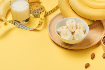 Measuring tape wrapped around a banana with almond on a yellow background, Concept of diet.
