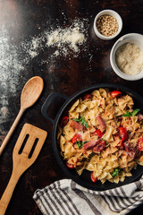 view from above of pasta with jamon, pine nuts, sauce, cherry tomatoes, mint leaves covered by grated parmesan in pan surrounded by kitchen towel, wooden spatula and spoon on table