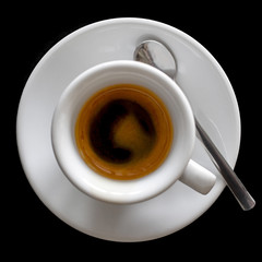 Small italian espresso in white ceramic cup with spoon isolated on black from above.