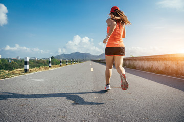 An asian woman athletic is jogging on the concrete road, she is warming her body and tideten her tying her shoes tightly fitting before workout.