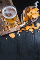 A glass of fresh beer with potatoe chips and peanuts on black background
