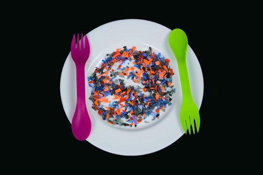Restrictions on the use of plastics.Food and Drink contains poisonous substances leaking from plastics.nCrushed multicolored plastic pieces on white plate and multifunctional cutlery.