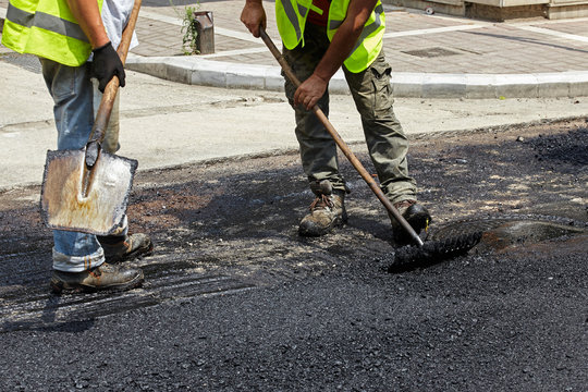 Workers using asphalt paver tools during road construction.
