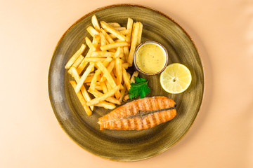 French fries and a piece of red fried fish salmon with a parsley leaf with sauce on a large plate....