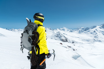 A mountaineer man holds an ice ax high in the mountains covered with snow. View from the back. outdoor extreme outdoor climbing sports using mountaineering equipment