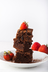 Stack of brownies decorated with strawberries on white plate on white background. Copy space.