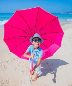 Boy with a pink umbrella on the sandy beach