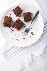 Brownie slices on a white plate on white napkin on white wooden background. Copy space. Flat lay. Overhead