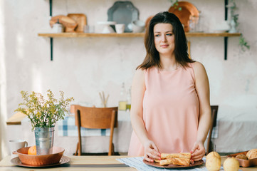 Young beautiful housewife in dress having breakfast on kitchen. Lovely woman posing and dreaming in country french style decorated interior zone. Rustic dining room with fresh food and tableware.