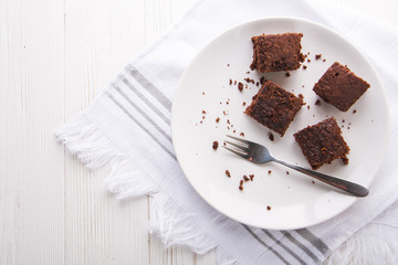 Brownie slices on a white plate on white napkin on white wooden background. Copy space. Flat lay. Overhead