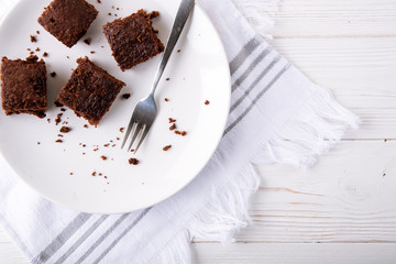 Brownie slices on a white plate on white napkin on white wooden background. Copy space. Flat lay. Overhead