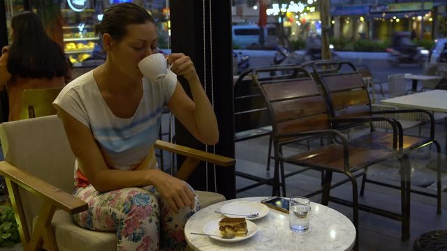 Woman sitting in coffee shop drinking coffee and eating tiramisu