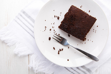 Brownie slice on a white plate on white napkin on white wooden background. Copy space. Flat lay. Overhead