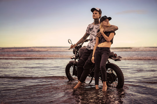 stylish couple standing and hugging near motorcycle on ocean beach