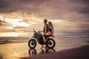 Fototapeta na wymiar boyfriend and girlfriend hugging on motorcycle at beach during sunrise