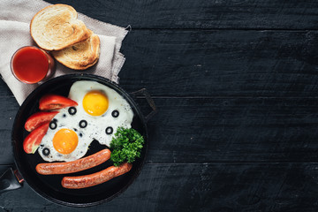 scrambled egg with sausages in the pan and tomatoe juice on black background. Copy space