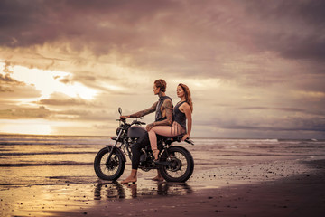 Fototapeta na wymiar affectionate couple sitting on motorcycle at beach during sunrise