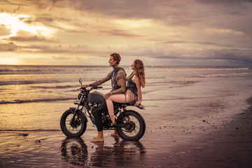 Fototapeta na wymiar tattooed boyfriend and girlfriend sitting on motorcycle at beach during sunrise