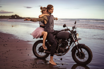 Obraz premium boyfriend sitting on motorcycle with open arms on ocean beach