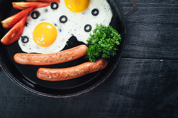 scrambled egg with sausages in the pan and tomatoe juice on black background. Copy space