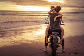 Obraz na płótnie Canvas heterosexual couple hugging on motorcycle on ocean beach during beautiful sunrise