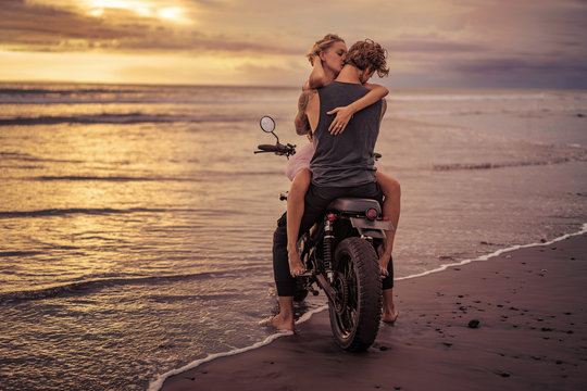 couple hugging on motorcycle on ocean beach during beautiful sunrise