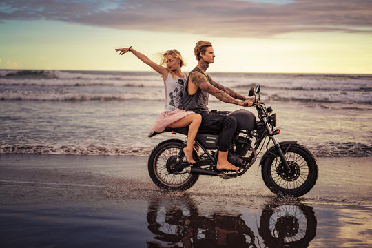 happy boyfriend and girlfriend riding motorbike on seashore during sunrise