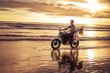 Fototapeta premium affectionate boyfriend and girlfriend riding motorcycle on ocean beach during sunrise