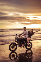 happy couple riding motorcycle on seashore during sunrise