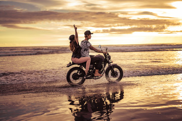 side view of couple riding motorcycle together on ocean beach during sunrise