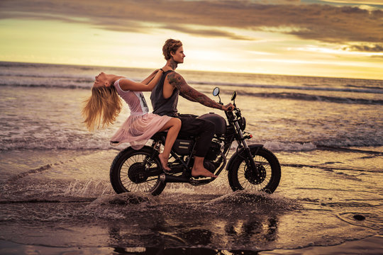attractive couple riding motorcycle on ocean beach during sunrise