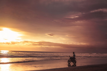 Obraz na płótnie Canvas man sitting on motorbike on seashore and looking at beautiful sunset