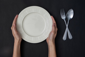 woman two hands hold a spoon and fork and white dish on black background