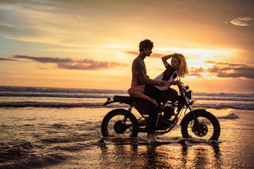 Fototapeta premium side view of passionate couple cuddling on motorbike at beach during sunset