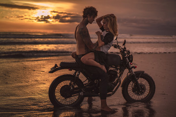 Obraz na płótnie Canvas sexy girlfriend and boyfriend cuddling on motorbike at beach during sunset