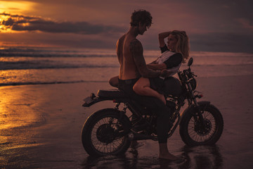 Fototapeta na wymiar seductive couple cuddling on motorbike at beach during sunset