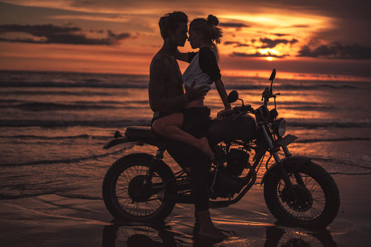 affectionate couple hugging and going to kiss on motorcycle at beach during sunset