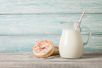 Glass pitcher with milk and donuts on wooden table