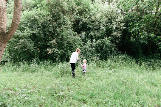 Woman and her young blonde daughter are picking wild flowers in the woods.
