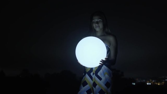 Attractive young happy woman staring and smiling and glowing ball at night 