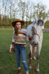 Beautiful young woman with white horse outdoors. Love animal. Cowgirl in jeans. Happy girl