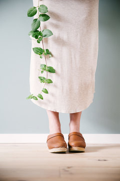 A woman holding a branch of Japanese honey suckle in bloom wearing neutral colors and brown leather clogs.