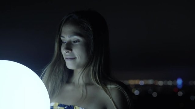 Attractive young happy woman holding glowing ball at night while smiling 