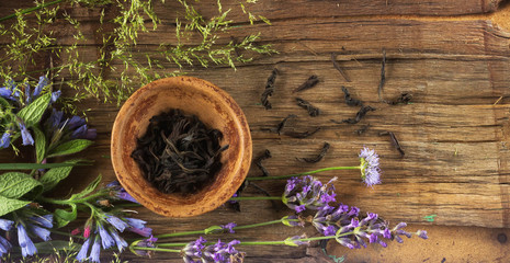 Petals of black tea in a small clay bowl, around the flowers of the field and twigs of lavana. Daylight. Top View