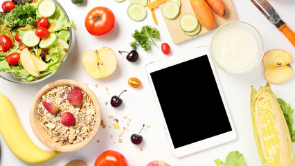 Top view of tablet with blank screen, mixed vegetables salad, muesli and fresh fruits on white background.