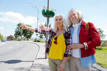 Hippy lifestyle. Aged hippy couple standing at the roadside while asking for a ride